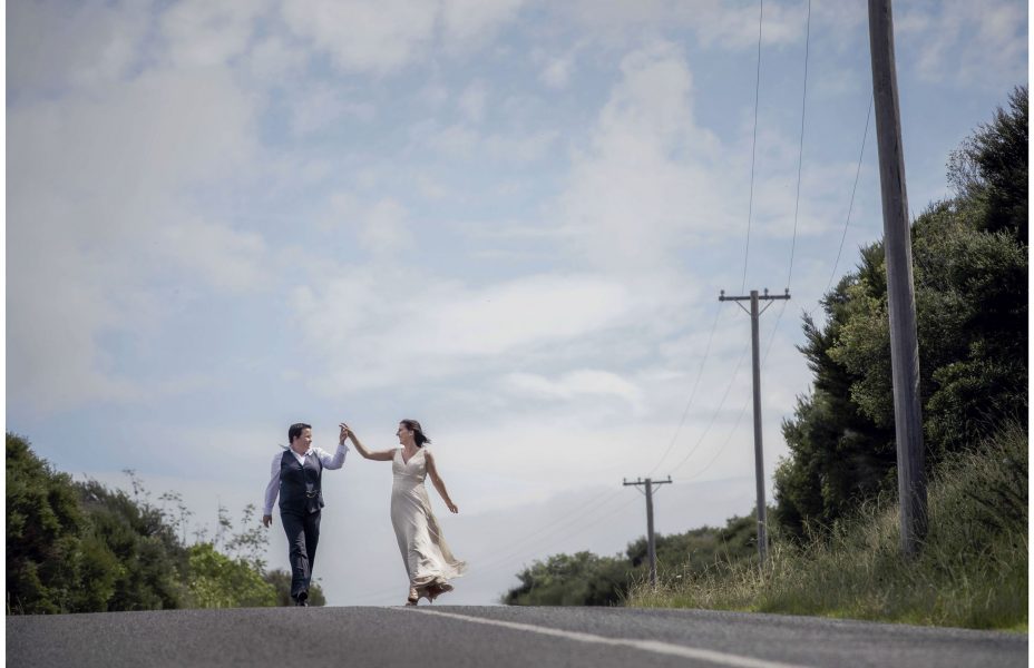 Same sex couple walk down the road together hand in hand in the sunshine on Waiheke Island
