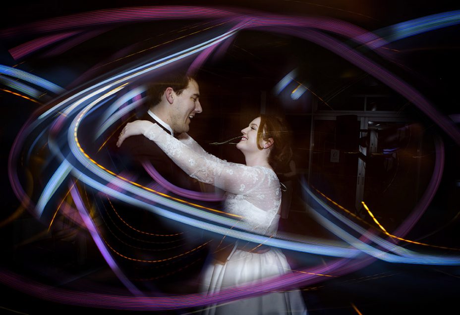 Capturing the moment.Wedding day bride wearing silk ivory coloured wedding dress and her new husband look into each other's eyes smiling during their first dance whilst surrounded by streaks of blue and purple light. .capturing the moment by Auckland Wedding photographer Chris loufte.