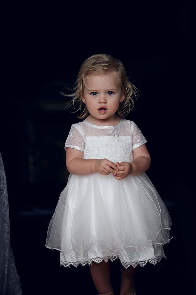 Cute flower girl wearing white sating dress has a startled expression as Auckland wedding photographer Chris Loufte captured the moment.