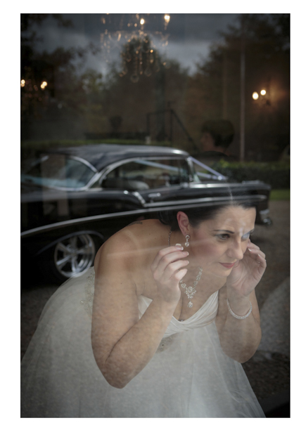 Bride adjusts her earing using her reflection in a windown