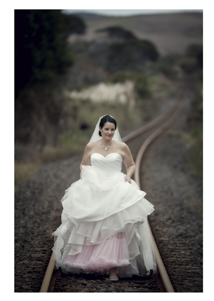Bride in wedding dress walking along romantic disused railway line in Kumeu.