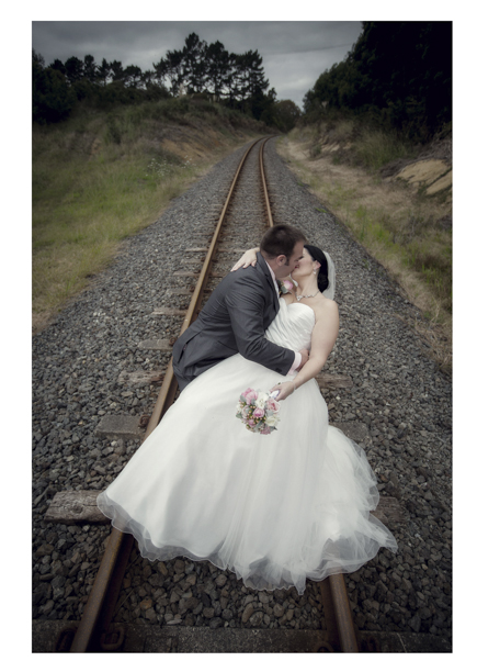 Bride in wedding dress embraces groom along romantic disused railway line in Kumeu.