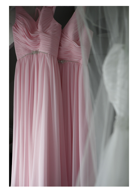bride's dress hangs next to with pink pleated bridesmaids dresses.