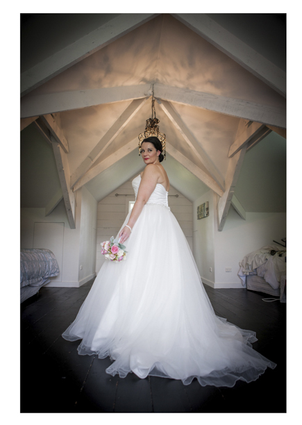Bride in fluu wedding dress poses for a photo in a room with a vaulted ceiling.