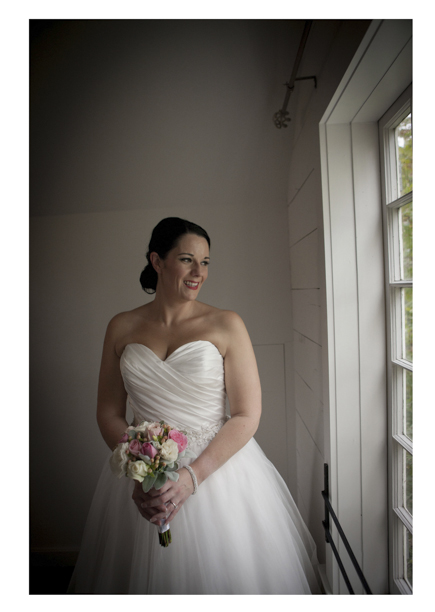 Bride in white dress poses for photo by window
