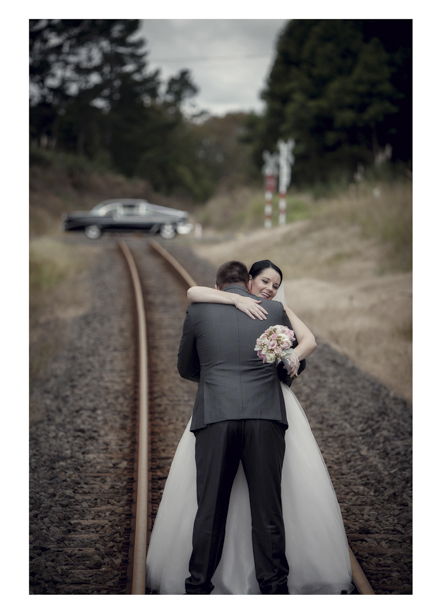 Bride in wedding dress embraces groom along romantic disused railway line in Kumeu.