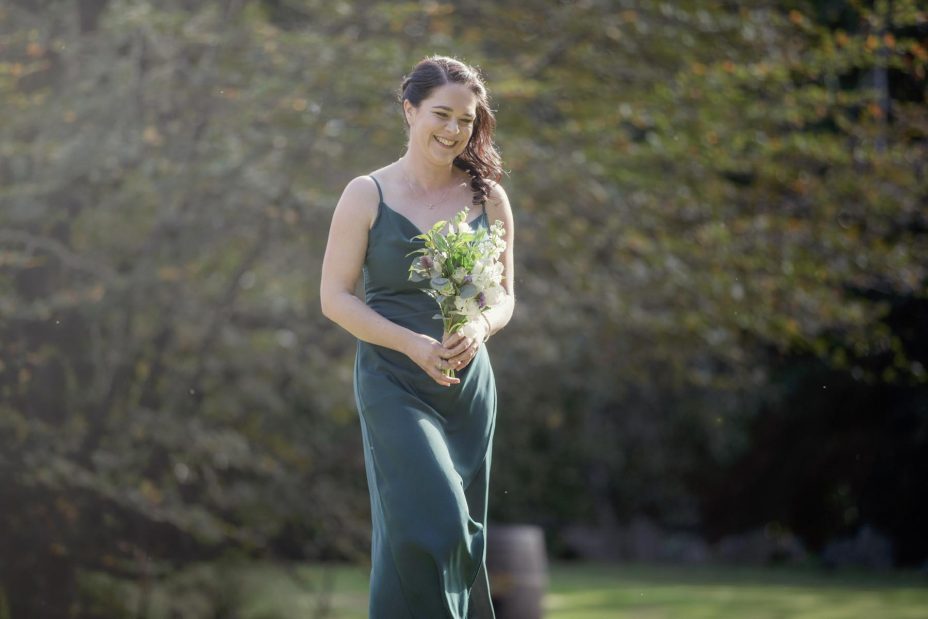 Bridesmaid in green dress wlaks slowly towards the ceremony