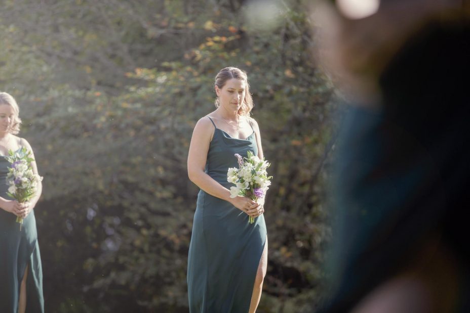 Bridesmaid in green dress wlaks slowly towards the ceremony