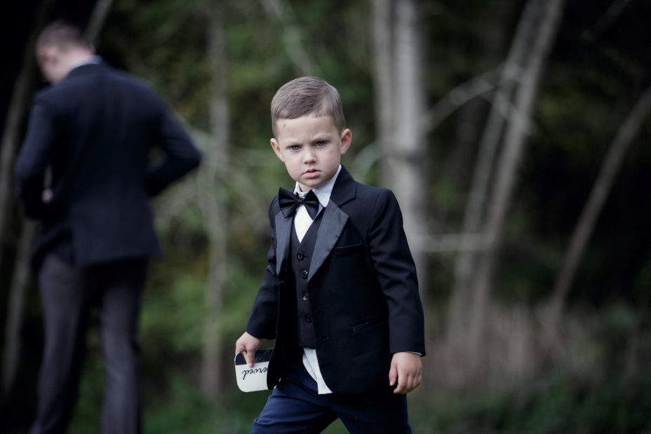 Little page boy wearing bow tie and black jacket at wedding