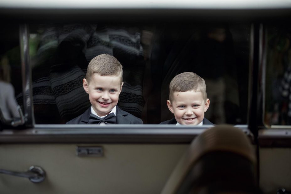 Two young page boys smiling framed by wedding car window