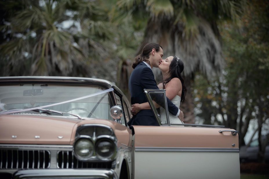 Bride and groom embrace next to their classic American wedding car