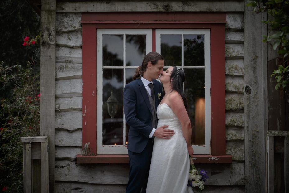 Bride and groom kiss infront of traditional wood window