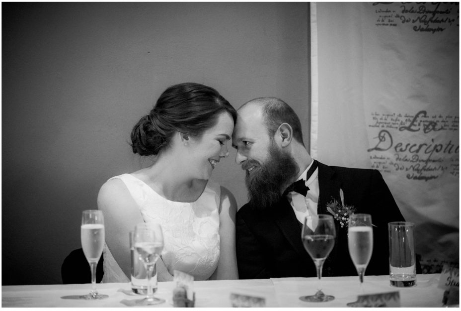 Bride and groom touch foreheads and smile as they listen to the speeches at their wedding reception at Mantells in Mount Eden.
