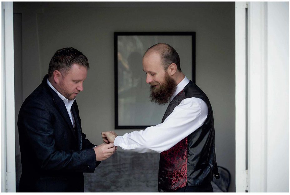 Best man helps wedding day groom put on some silver cuff-links.