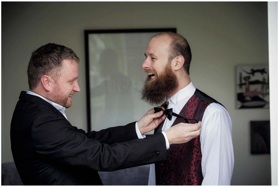Best man helps wedding day groom to tie a proper bow tie.