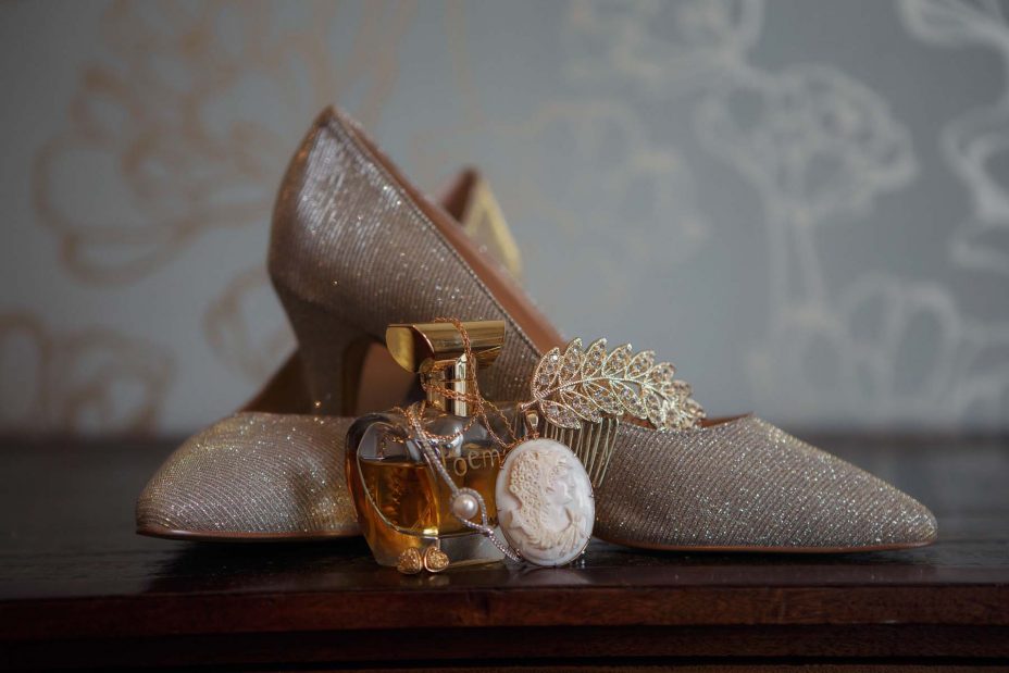 Sparkling gold Wedding shoes. On an antique wooden table top with bride's perfume and jewellery in a bedroom at Mount Eden Villa.