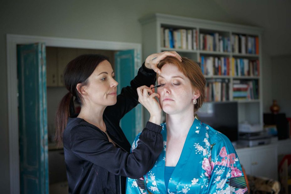 Bridesmaid wearing light blue floral kimono robe has her wedding make up applied at Mount Eden Villa.