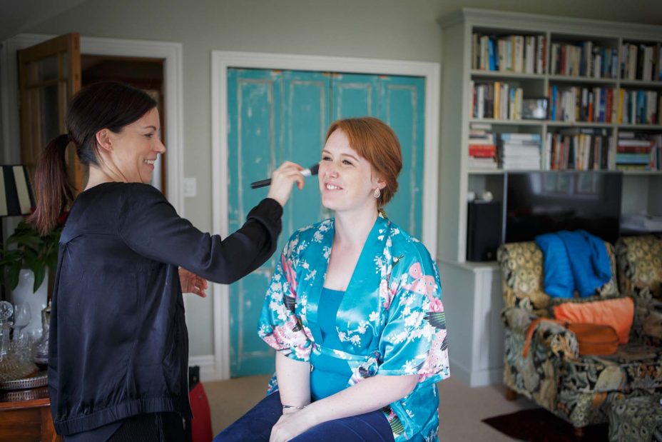 Bridesmaid wearing light blue floral kimono robe has her wedding make up applied at Mount Eden Villa.