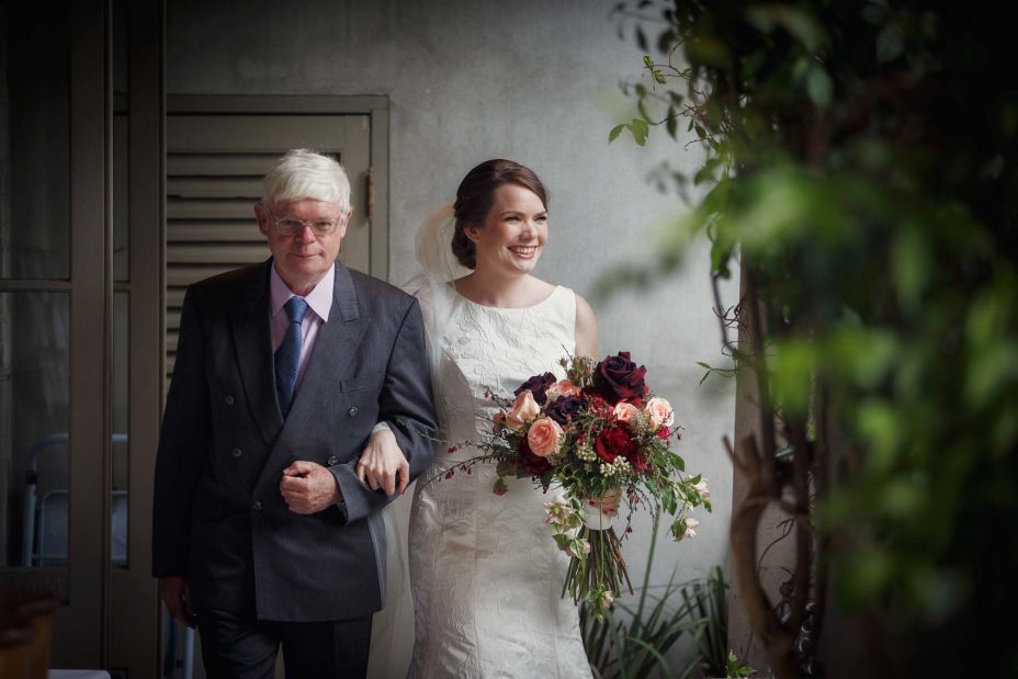 Bride and her father walk arm in arm down the isle towards her wedding ceremony at Mantells Mount Eden.