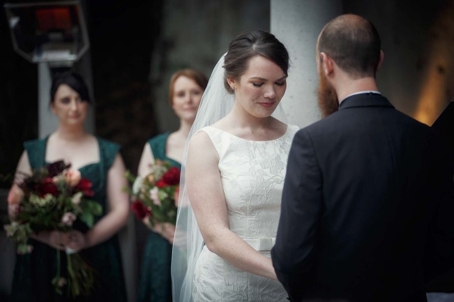 Smiling happy bride looks down during at her wedding ring during her wedding ceremony .