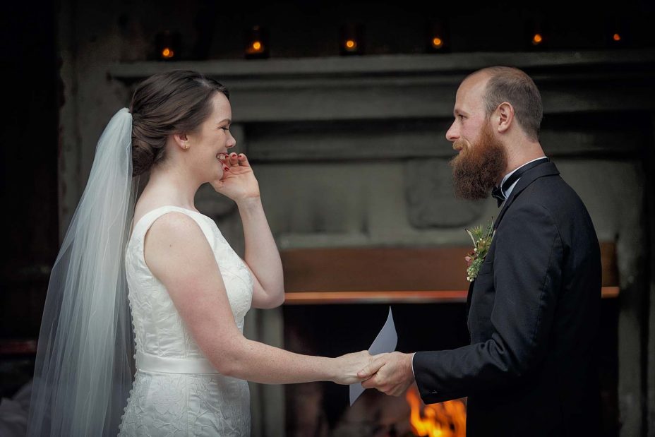 Smiling, happy bride and groom hold hands in front of the fireplace at Mantells in Mount Eden.