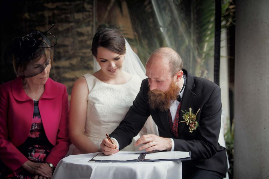 Wedding day groom sits and completes the wedding register following the ceremony at Mantells in Mount Eden.
