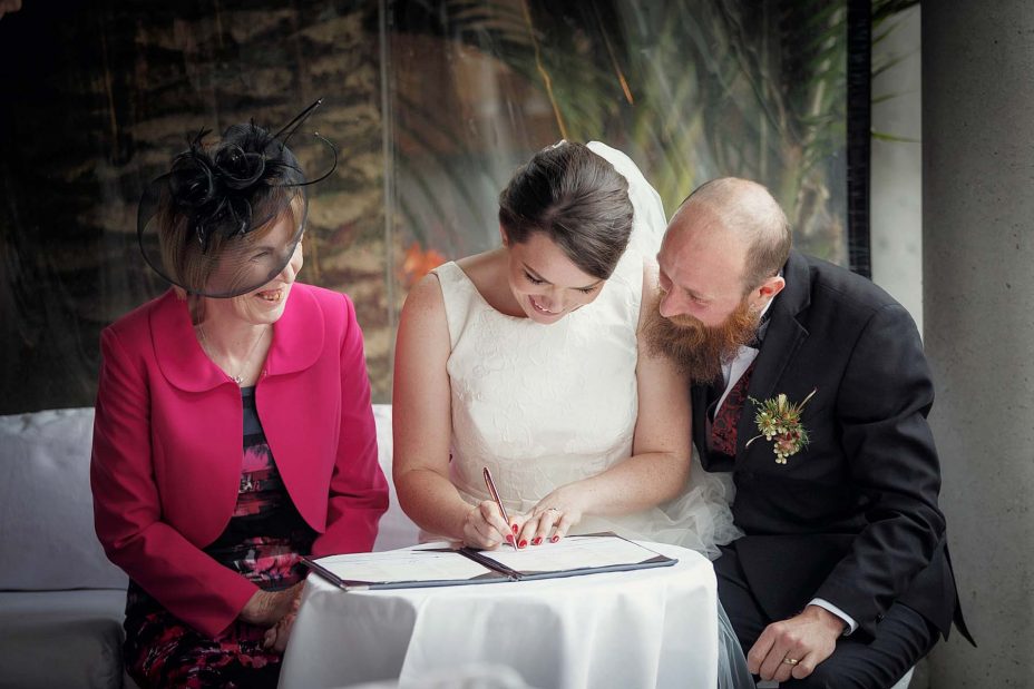 Bride and groom sit and complete their wedding register following their ceremony at Mantells in Mount Eden.