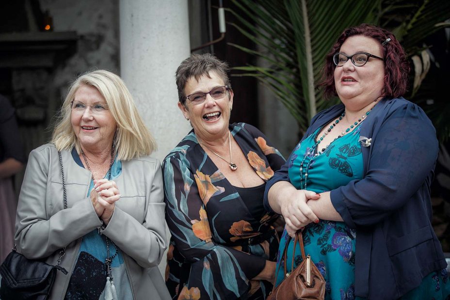 Wedding guests laugh together after the wedding ceremony in front of the fireplace at Mantells in Mount Eden.