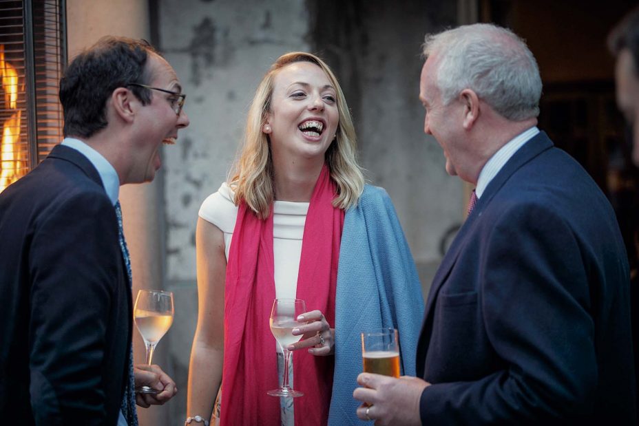 Wedding guests holding drinks laugh together after the wedding ceremony in front of the fireplace at Mantells in Mount Eden.
