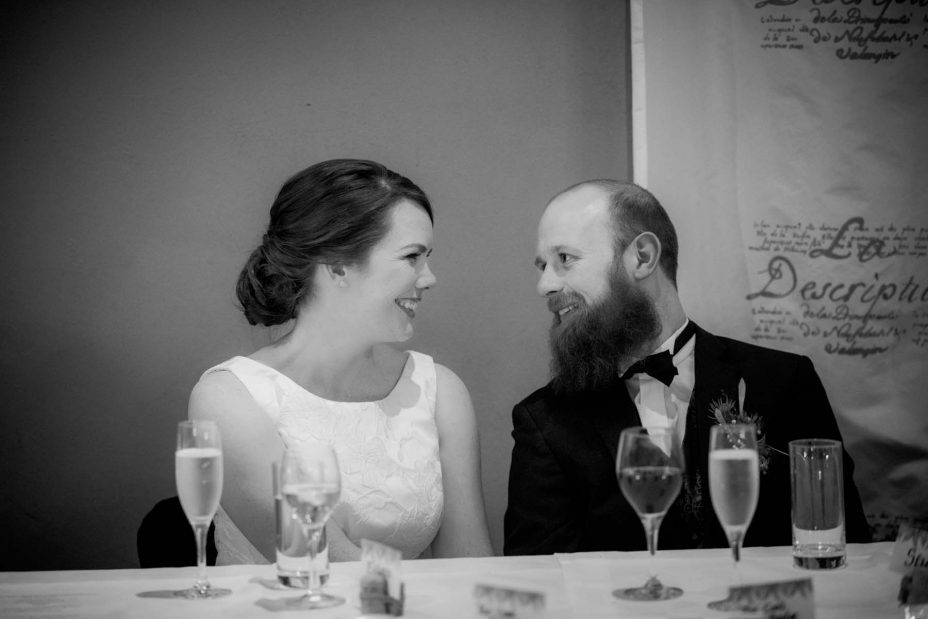 A loving moment captured as bride and groom gaze into each other's eyes and smile whilst they listen to the speeches at their wedding reception at Mantells in Mount Eden.