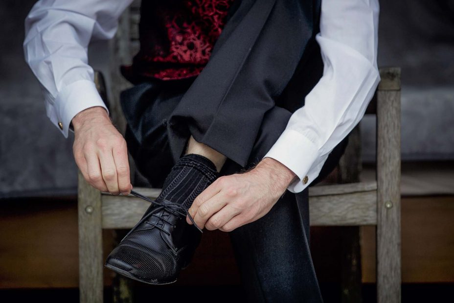Wedding day groom ties the laces on his formal black wedding shoes.