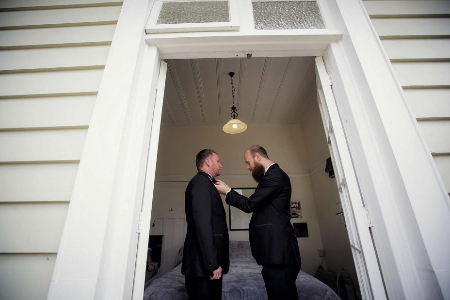 Wedding day groom helps his best man with his bowtie as they prepare for the wedding ceremony at Mantells in Mount Eden.