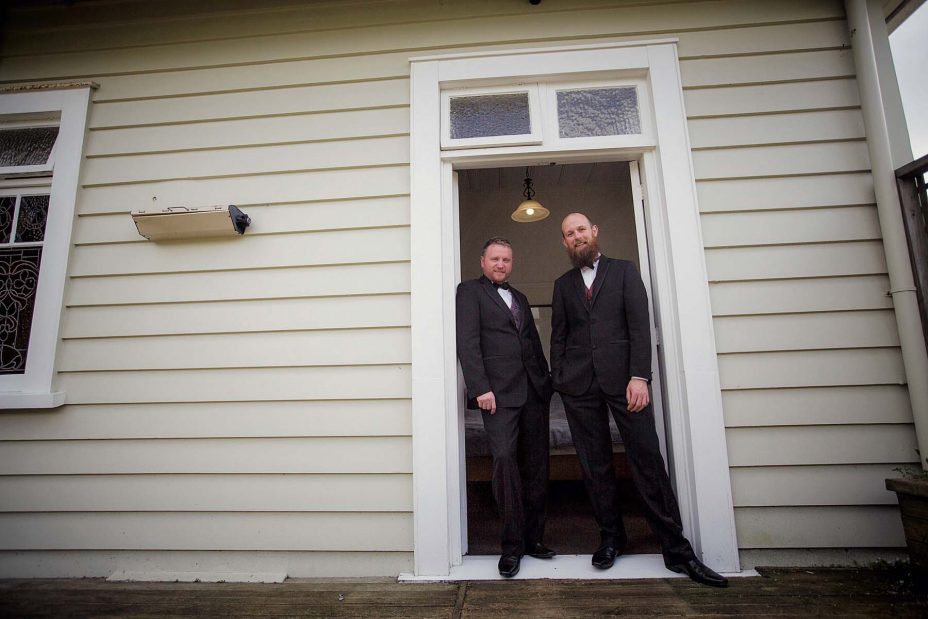 Wedding day groom helps his best man stand in the doorway of an old weatherboard villa as they prepare for the wedding ceremony at Mantells in Mount Eden.