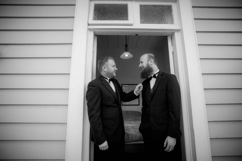 Wedding day groom helps his best man stand in the doorway of an old weatherboard villa as they prepare for the wedding ceremony at Mantells in Mount Eden.Black and white photo.