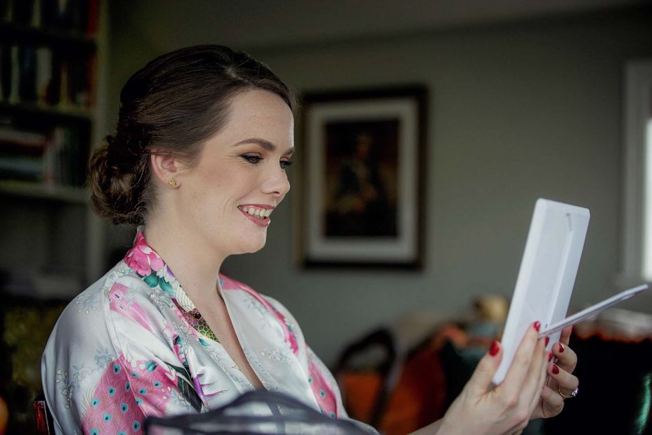 Wedding day floral kimono robe looks at herself in a small mirror as she has her wedding make up applied at Mount Eden Villa.