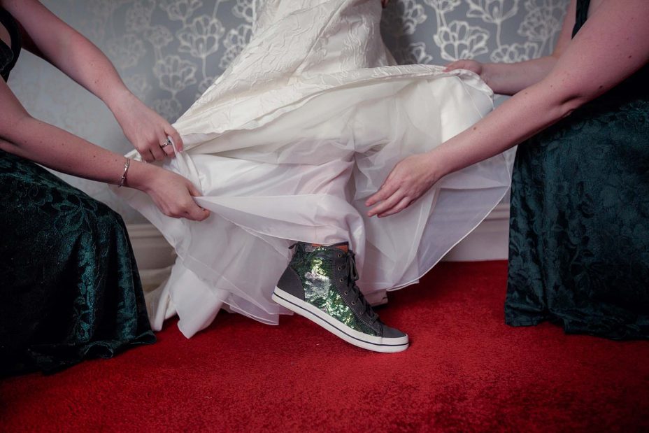 Bridesmaids lift the bottom of the bride's classical white wedding dress to reveal her unusual sparkling green wedding boots.