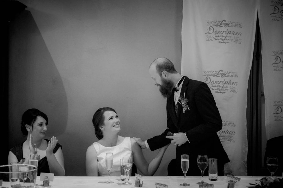 Bride and groom touch each other whilst gazing into each other's eyes as groom makes his speech during their wedding reception at Mantells in Mount Eden.