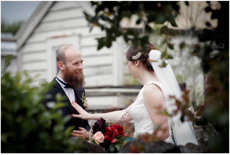 Wedding day groom smiles happily as his bride to be as she reveals herself in her wedding dress for the first time in the garden at Mount Eden Villa.