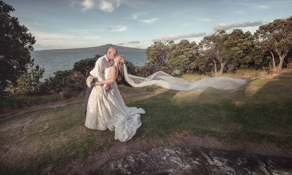 sunset wedding photo of bride and groom kissing in front of Rangitoto at fort takapuna