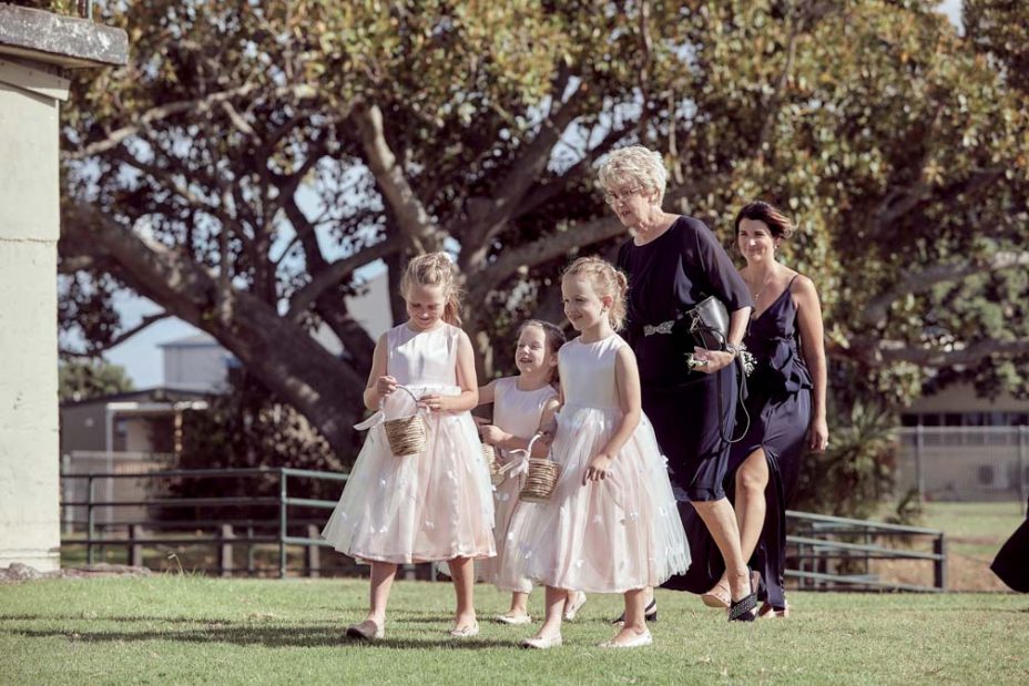 Little flower girls wearing matching pink dresses spread rose petals for the bride before a wedding ceremony at Fort Takapuna and the Officers Mess in Auckland.