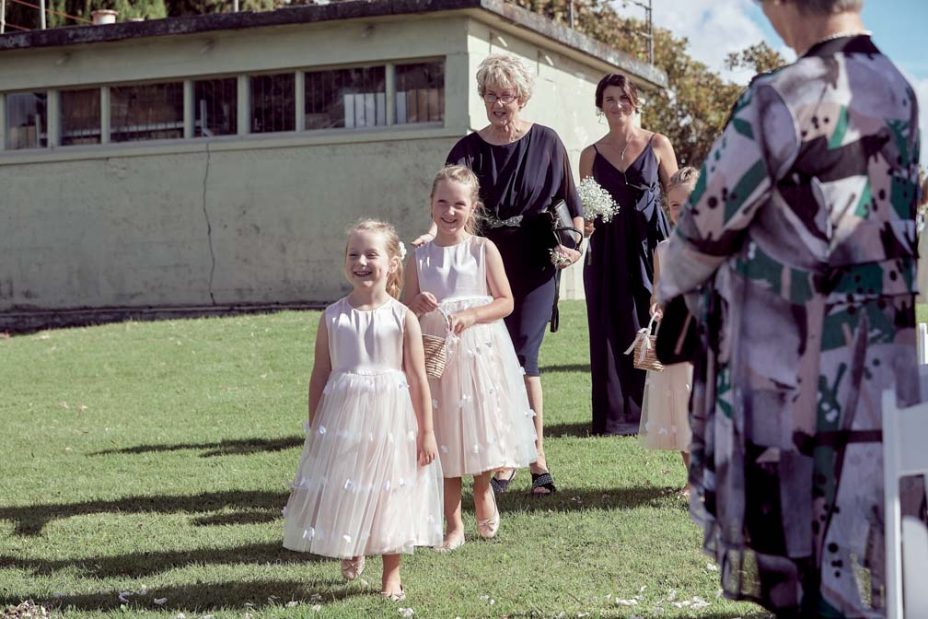 Little flower girls wearing matching pink dresses spread rose petals for the bride before a wedding ceremony at Fort Takapuna and the Officers Mess in Auckland.
