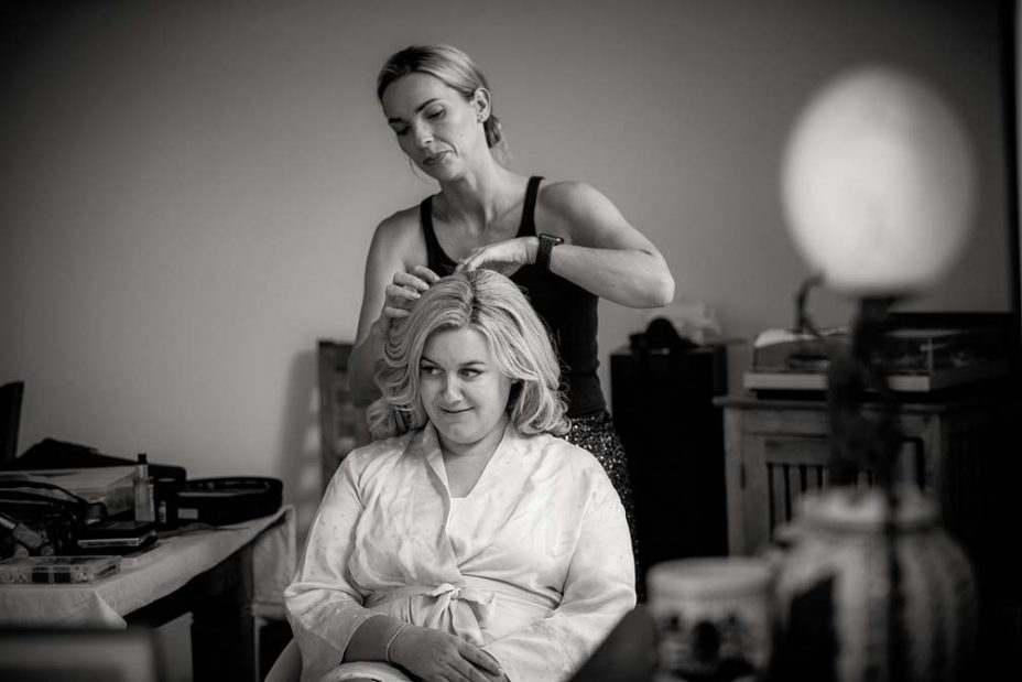 Black and white photo of a wedding day bride discussing hairstyles with has makeup artist as they get ready for her wedding ceremony and reception at Fort Takapuna and the Officers Mess in Auckland.