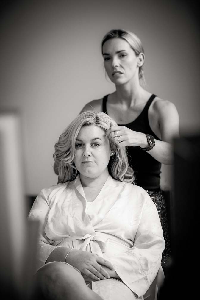 Black and white photo of a wedding day bride discussing hairstyles with has makeup artist as they get ready for her wedding ceremony and reception at Fort Takapuna and the Officers Mess in Auckland.