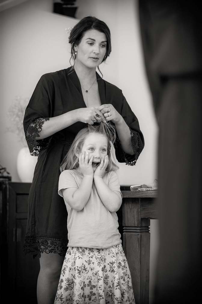 Black and white photo of a little flower girl with and excited expression on her face has her hair is platted in preparation for a wedding at Fort Takapuna and the Officers Mess in Auckland.