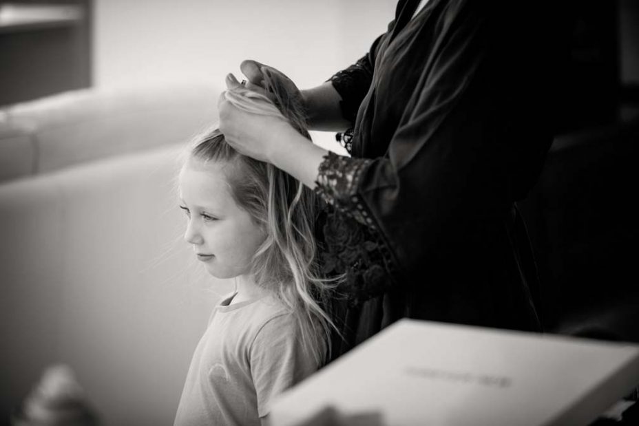 Black and white photo of a little flower girl standing as her hair is platted in preparation for a wedding at Fort Takapuna and the Officers Mess in Auckland.