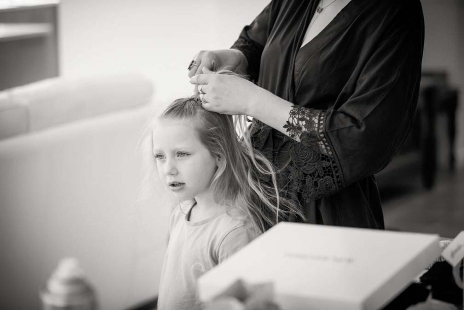 Black and white photo of a little flower girl standing as her hair is platted in preparation for a wedding at Fort Takapuna and the Officers Mess in Auckland.