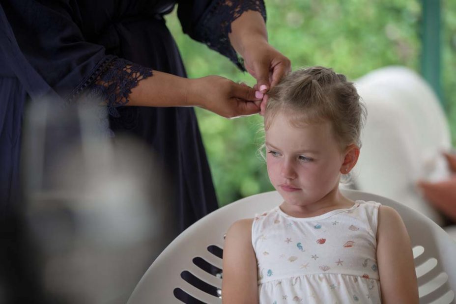 A little flower girl sits dreaming in a chair as her hair is platted as she prepares for a wedding at Fort Takapuna and the Officers Mess in Auckland.