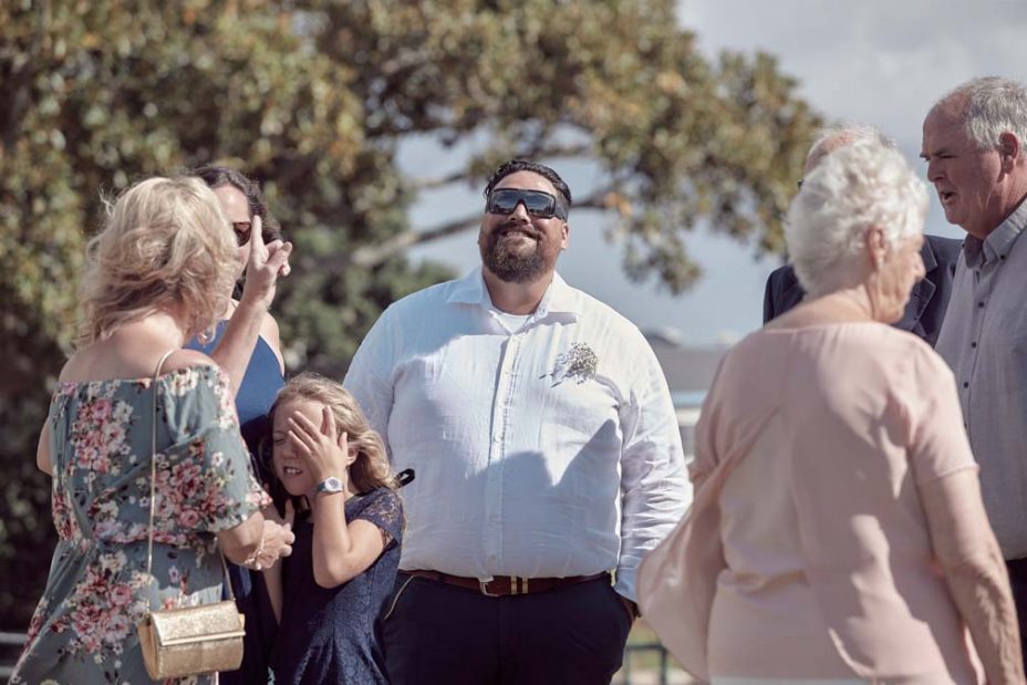 Wedding guests laughing in the sunshine following a wedding ceremony at Fort Takapuna in Auckland.