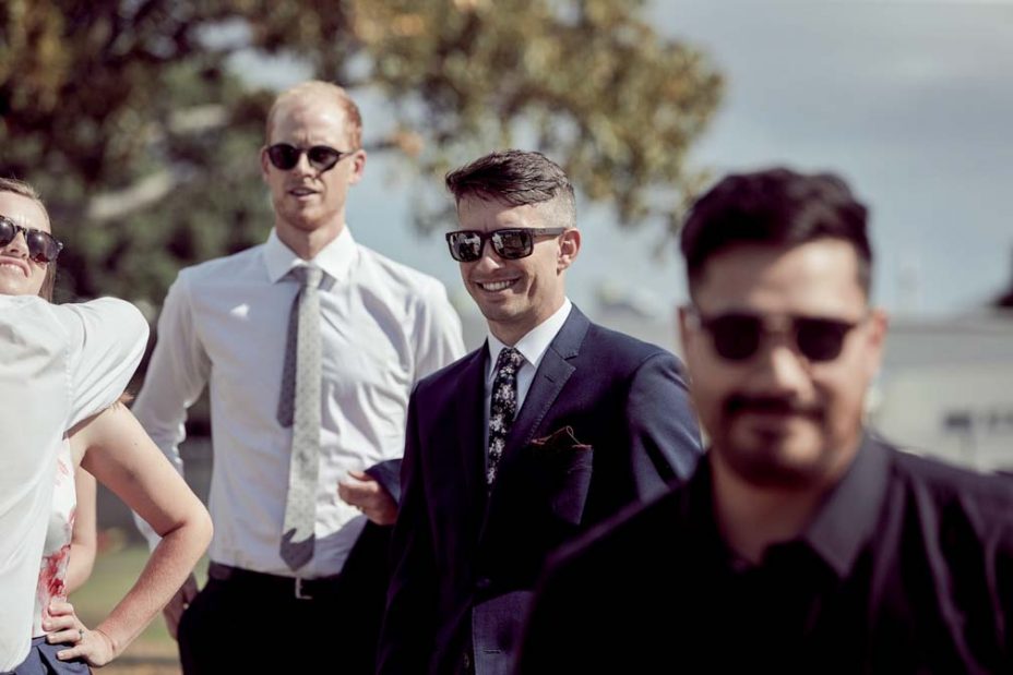 Wedding guests laughing in the sunshine following a wedding ceremony at Fort Takapuna in Auckland.