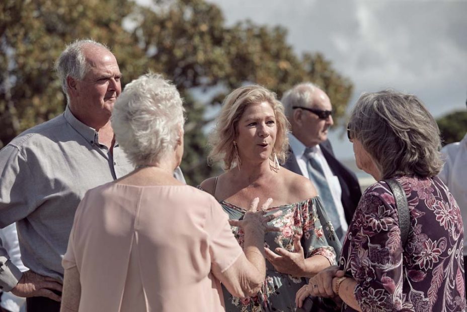 Wedding guests laughing in the sunshine following a wedding ceremony at Fort Takapuna in Auckland.